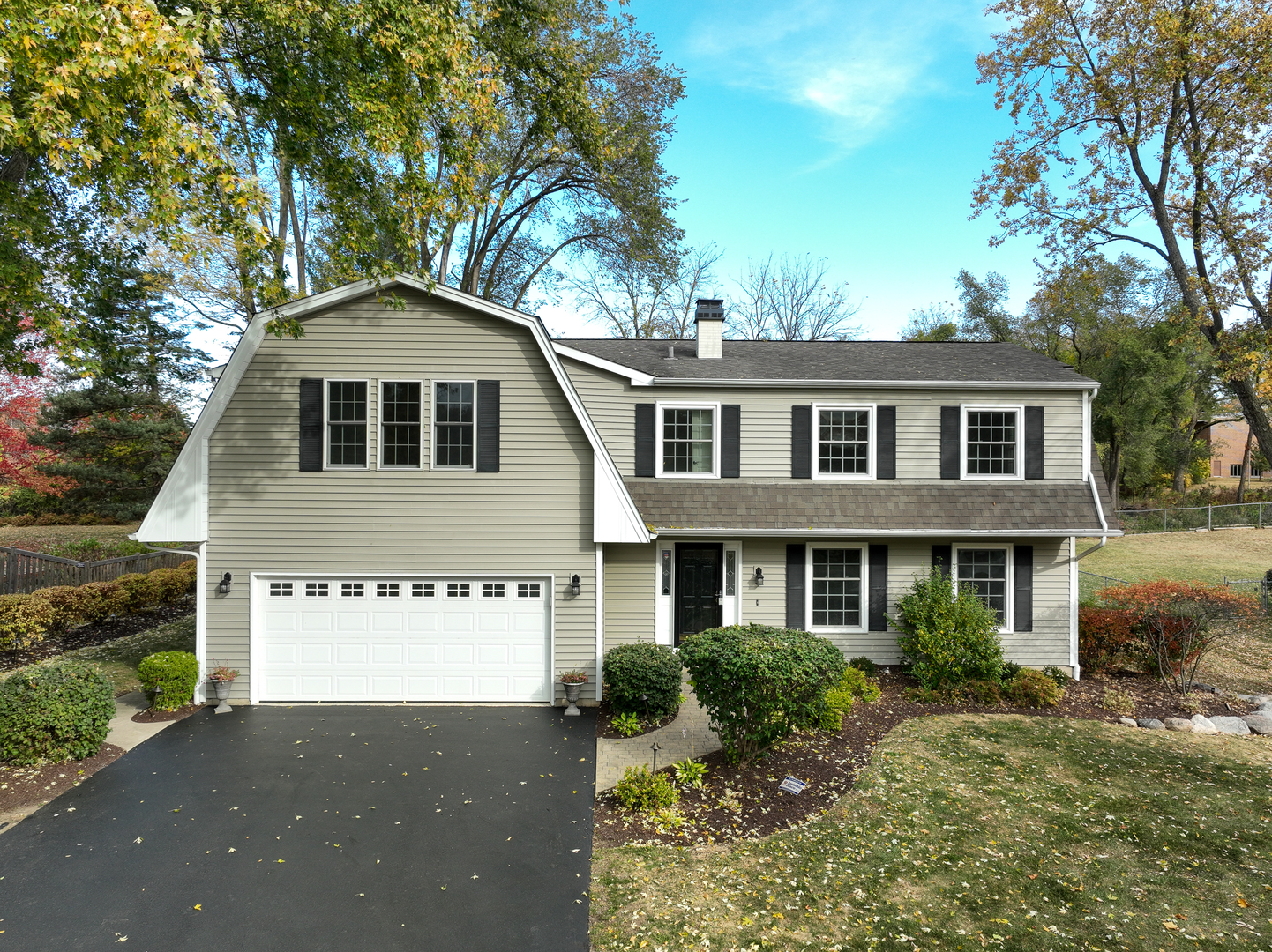 Gray split-level home with black shutters, attached two-car garage, and landscaped front yard.