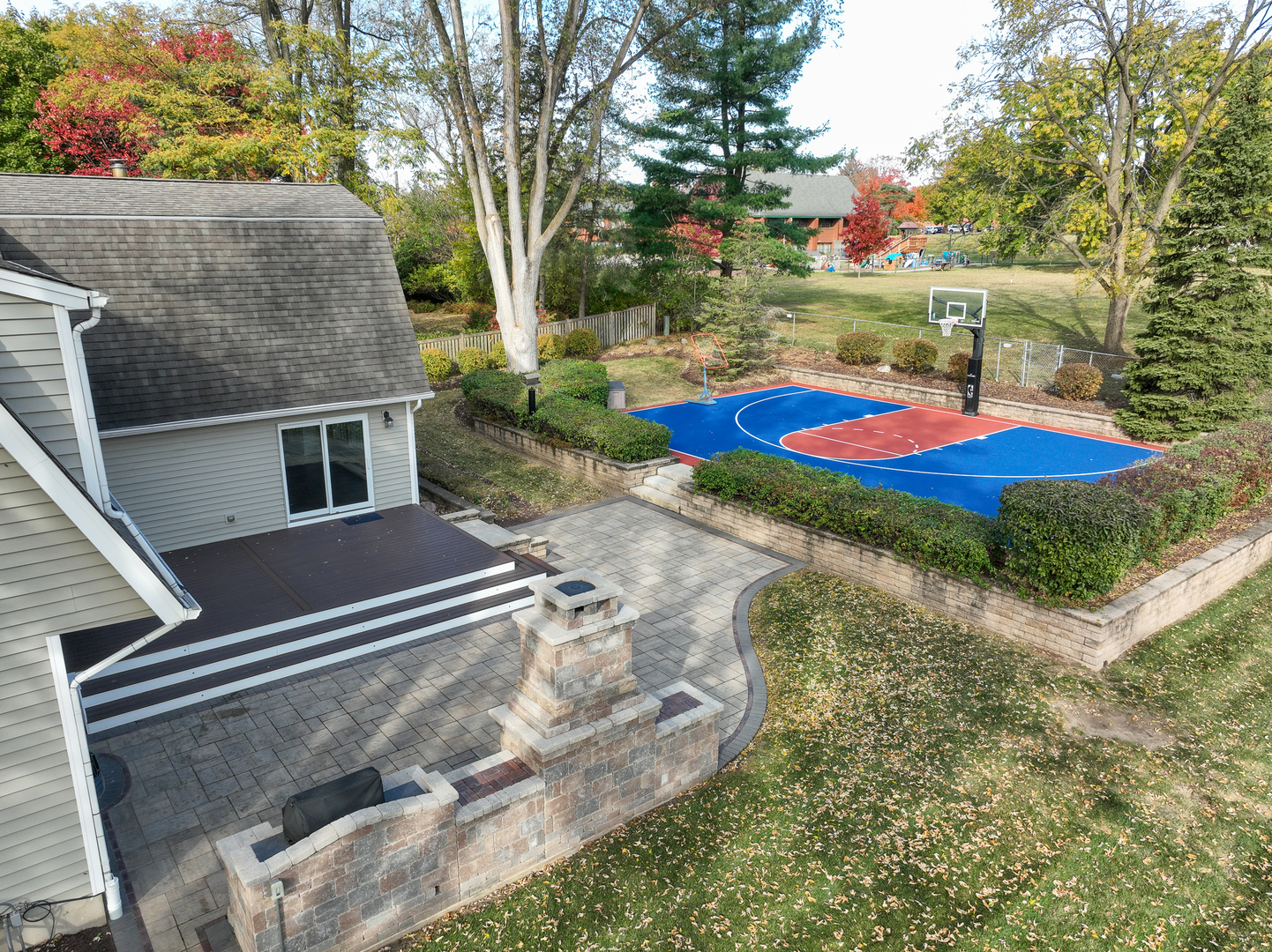 Backyard patio and basketball court surrounded by mature autumn trees.