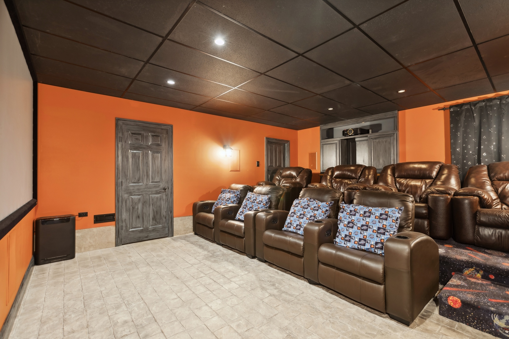 Home theater with brown leather recliners, orange walls, and a ceiling-mounted projector.