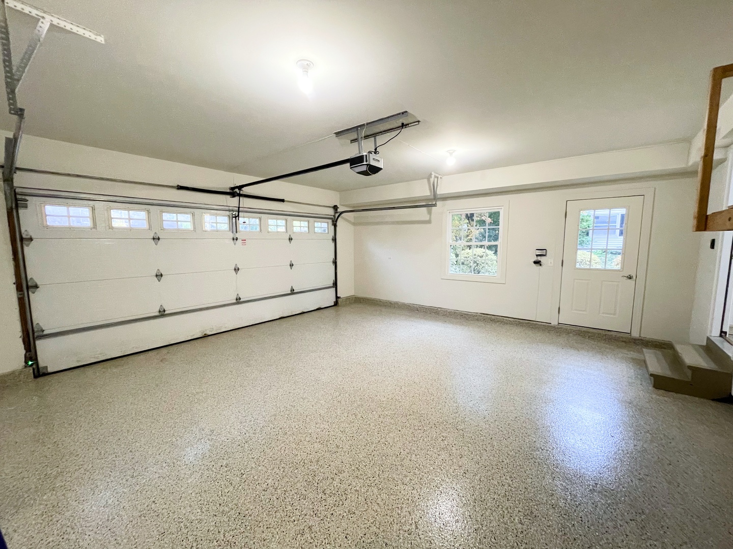 Empty garage with a speckled floor, overhead door, window, and side entry door.
