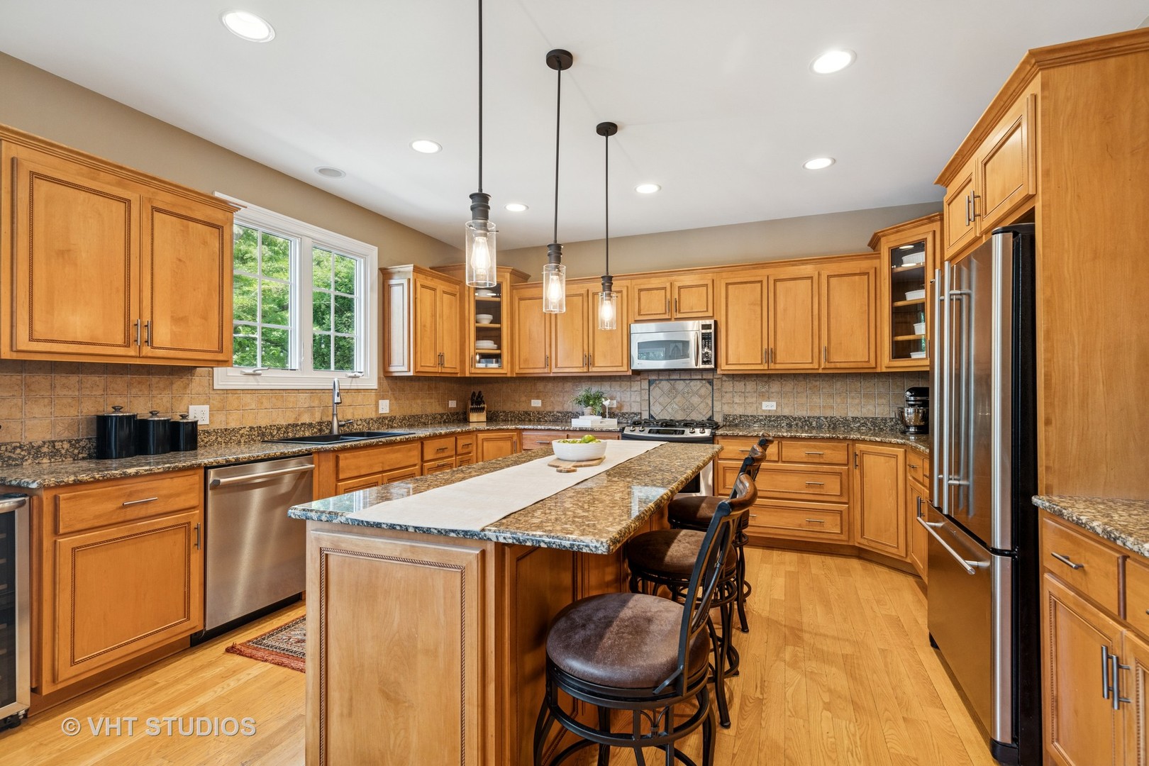 Kitchen with a large granite island, honey-toned cabinetry, and stainless steel appliances.