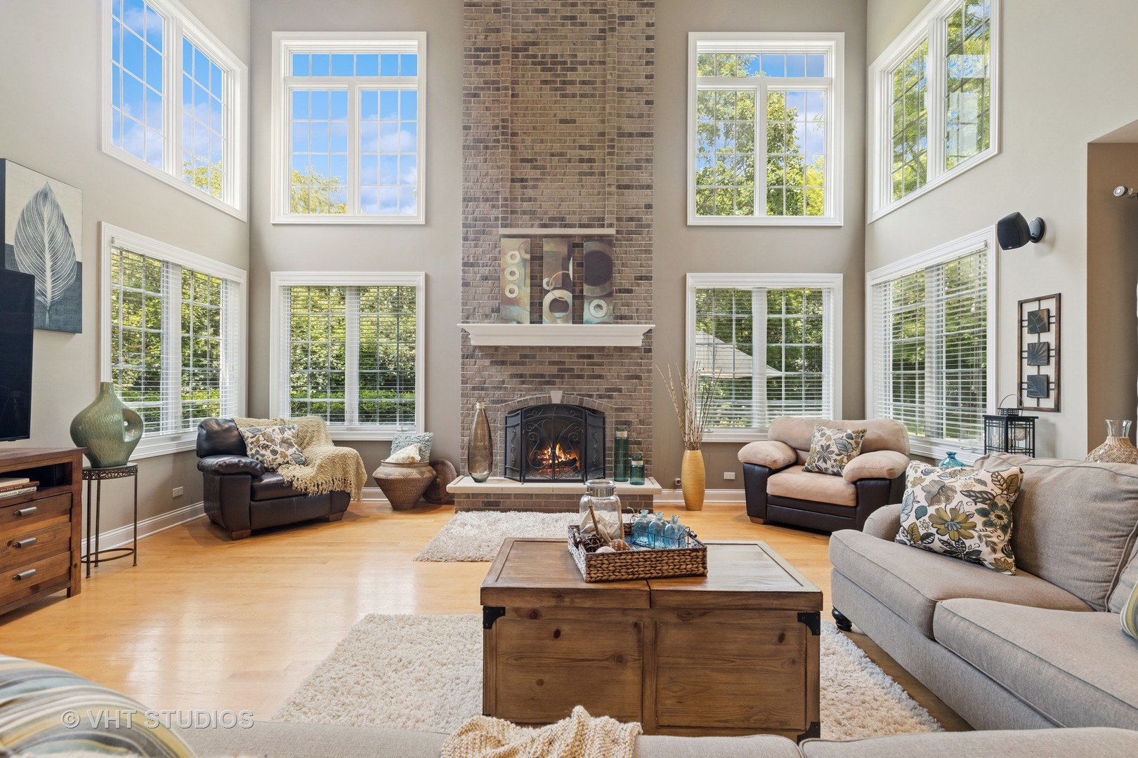 Two-story living room with a tall brick fireplace, large windows, and hardwood floors.