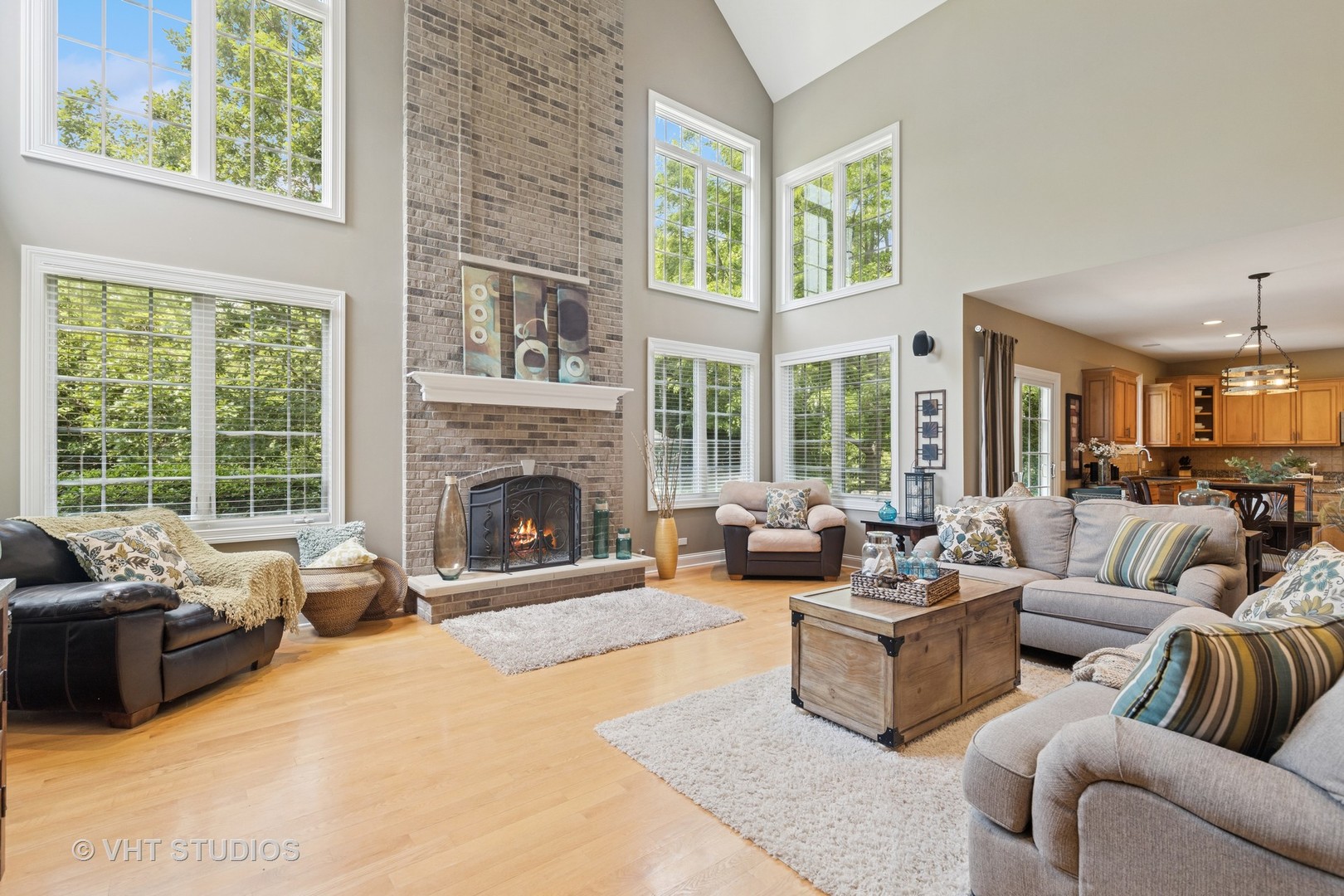 Vaulted living room with a tall brick fireplace, expansive windows, and hardwood floors.