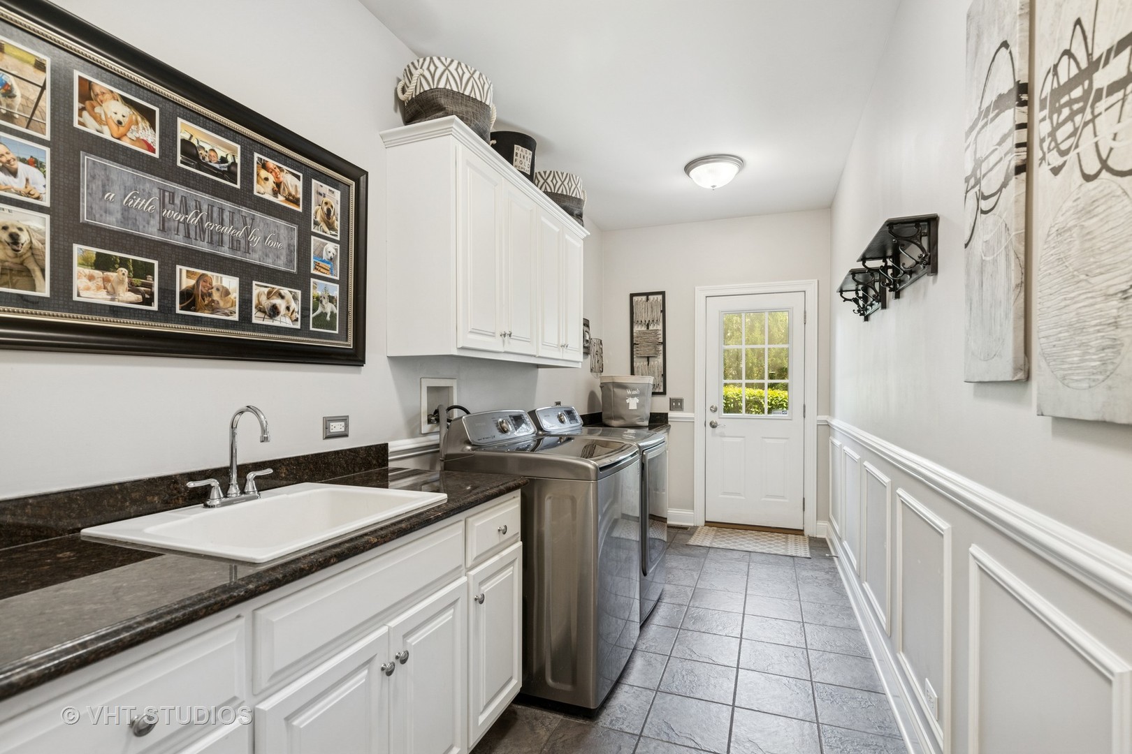 Laundry room with a utility sink, stainless steel washer and dryer, white cabinetry, and a glazed exterior door.