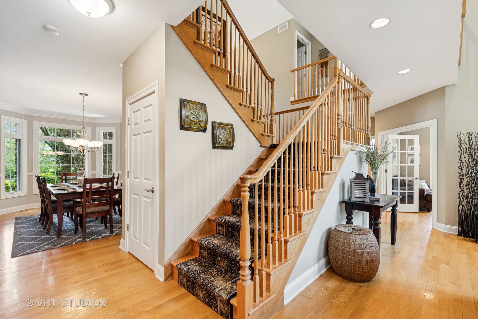Foyer with a carpeted staircase and wood railings beside a window-lit dining room.