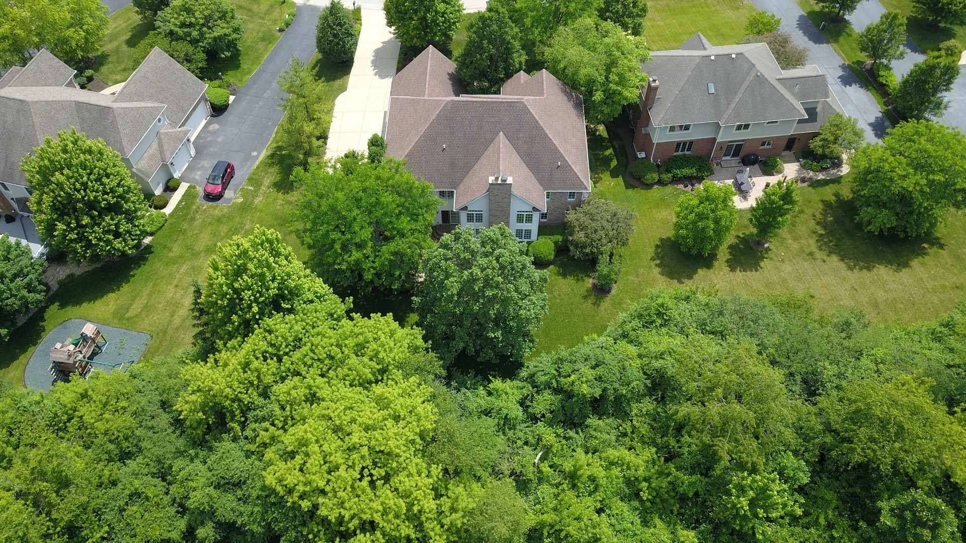 Aerial view of a two-story home surrounded by mature trees, with a small playground nearby.