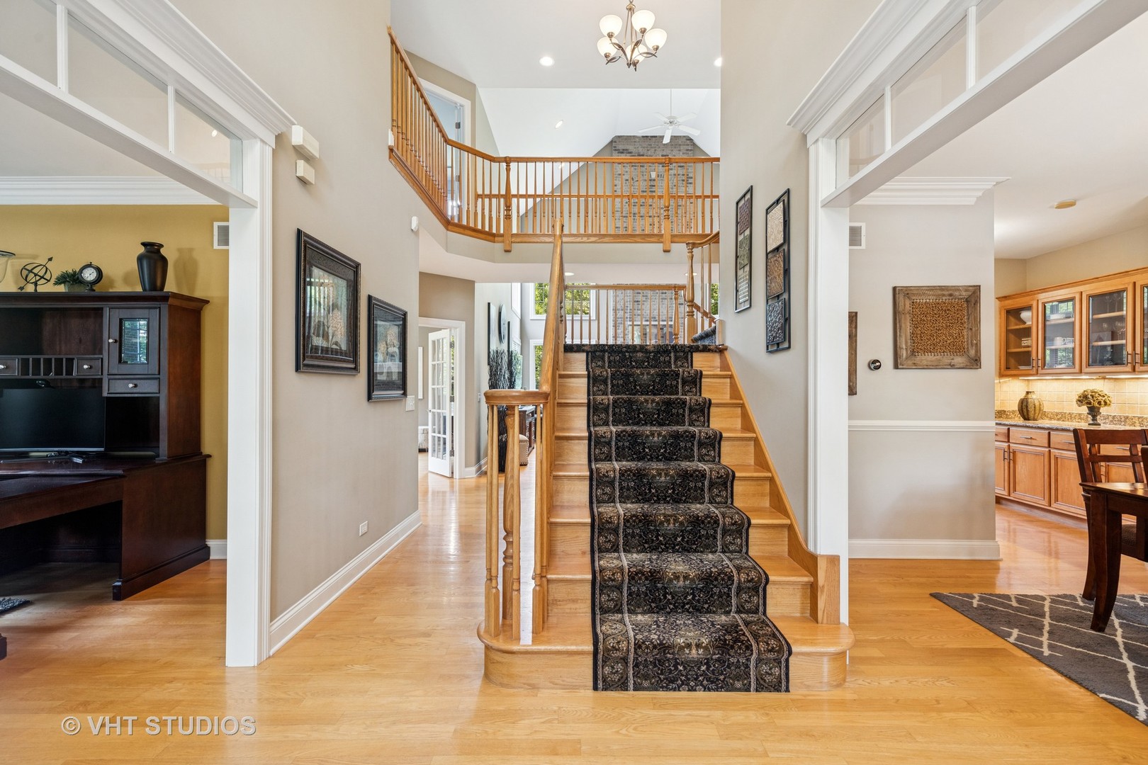 Two-story foyer with a wood staircase, patterned runner, and hardwood floors.