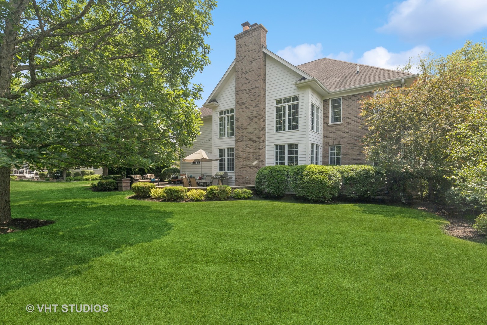 Rear of a brick-and-siding home with a tall chimney, patio seating, and a spacious lawn.