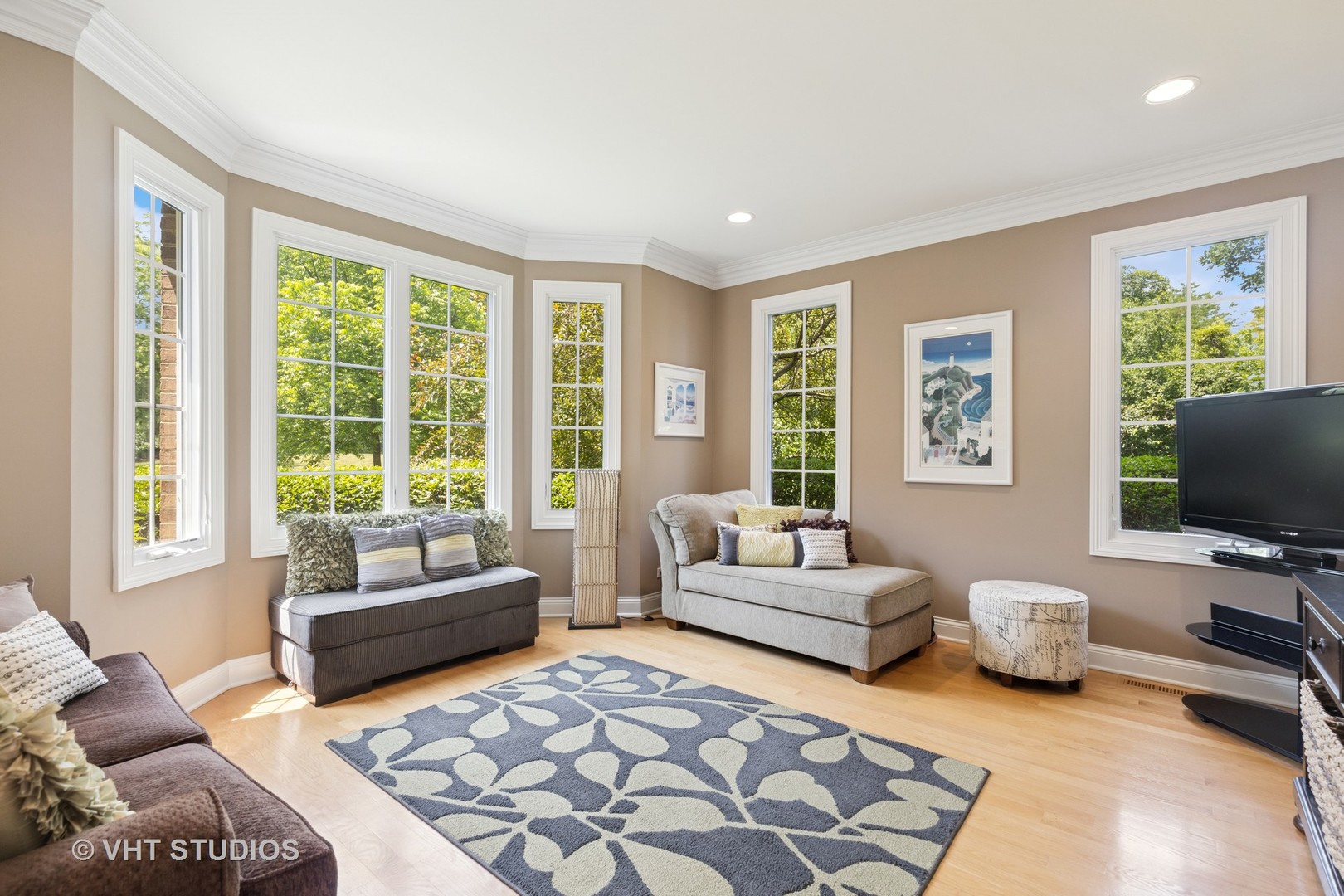 Living room with multiple windows, upholstered seating, hardwood floors, and a blue patterned rug.