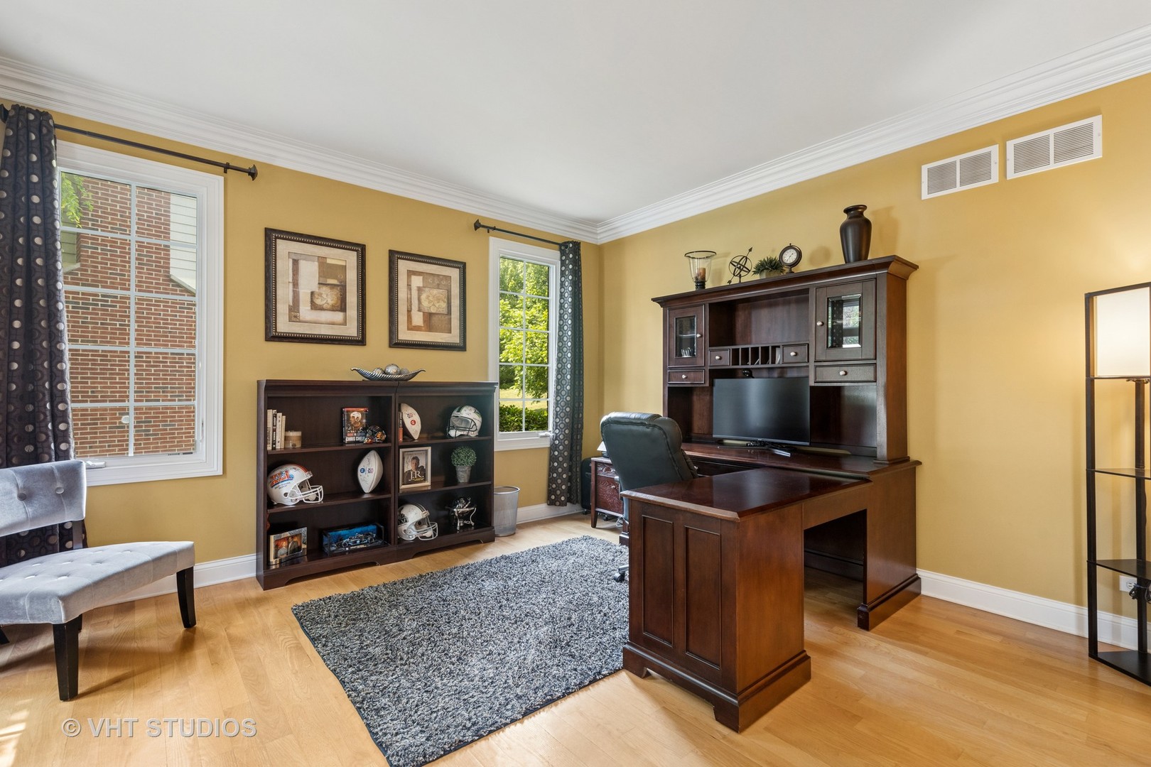 Furnished home office with a dark wood desk, football memorabilia, and mustard-yellow walls.