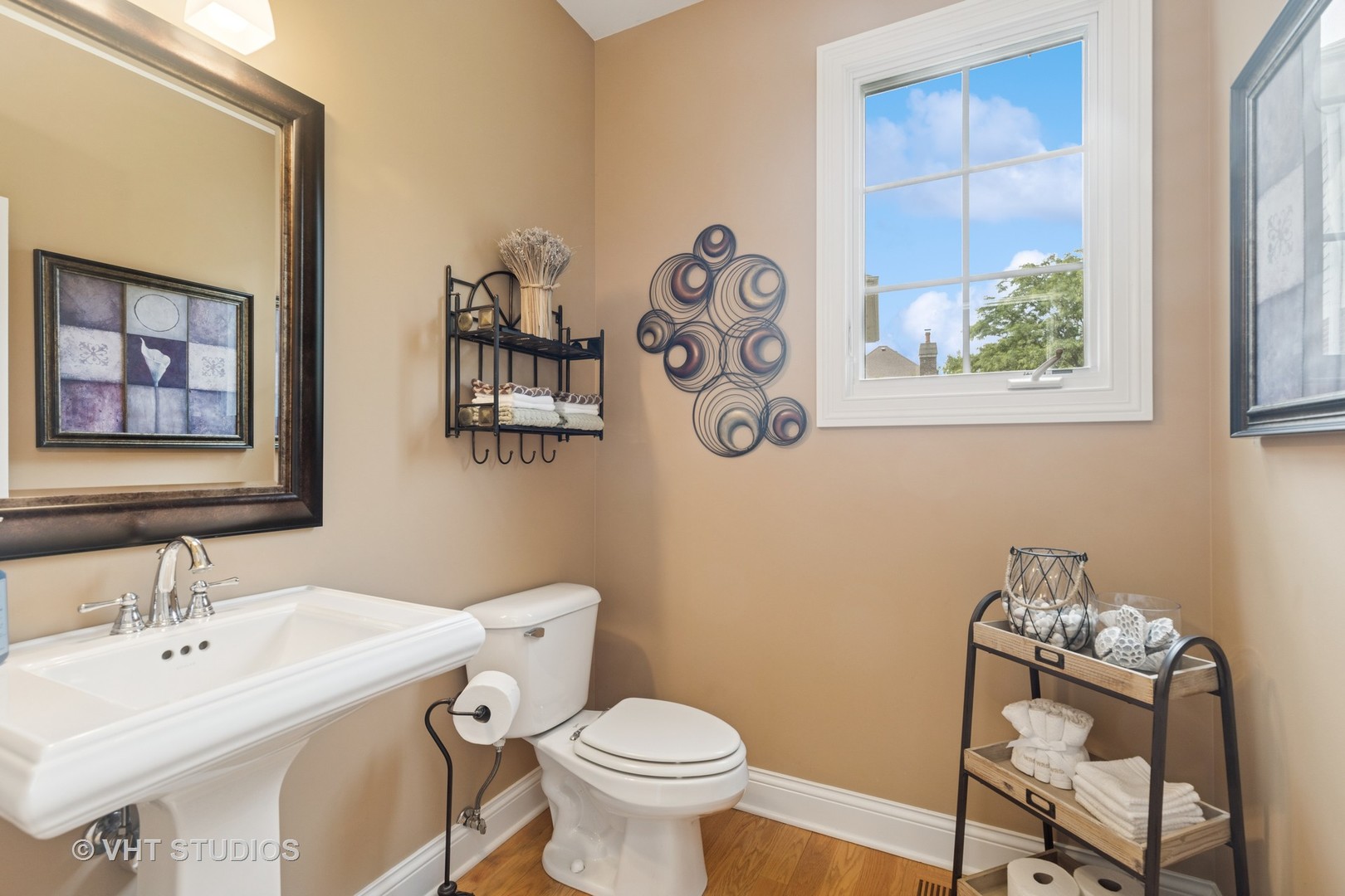Powder room with a pedestal sink, toilet, warm beige walls, and a large window.