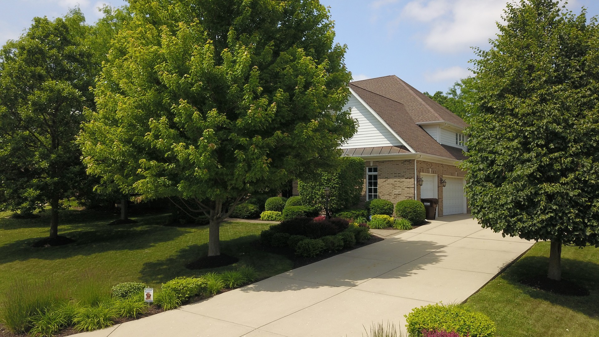 Two-story brick and white-sided home with an attached garage, broad driveway, and mature landscaping.