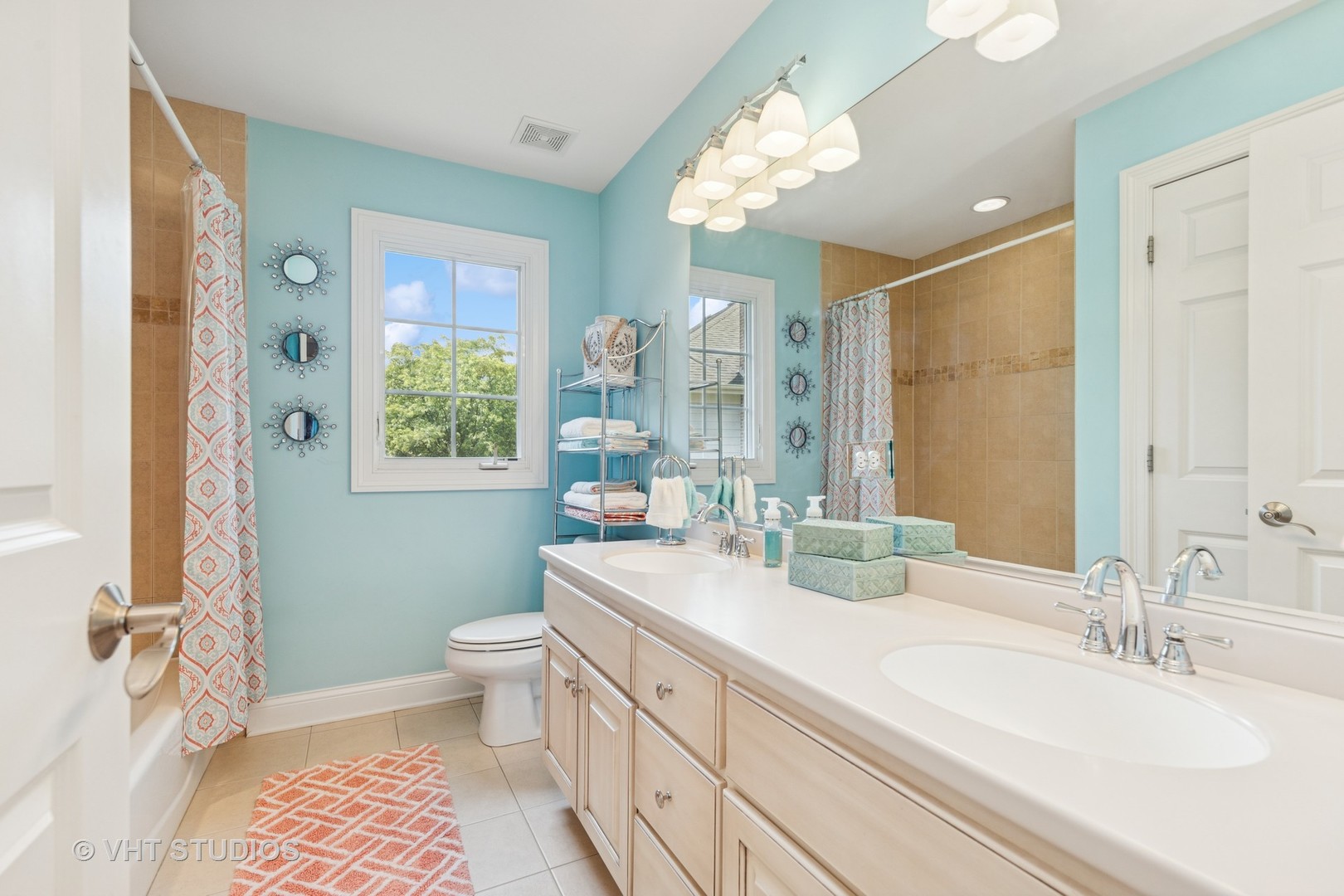 Bathroom with a double-sink vanity, turquoise walls, tan tile, and patterned shower curtains.