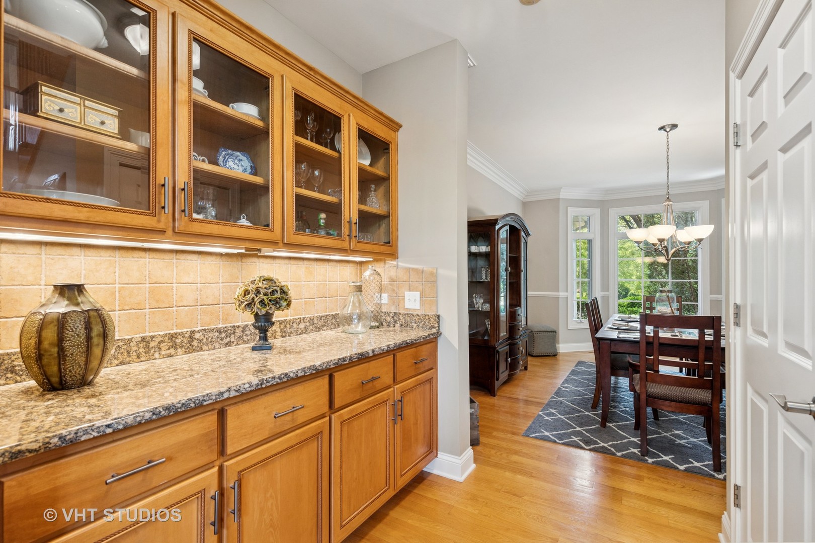 Kitchen with glass-front wood cabinets and granite counters opening to a bright dining area.