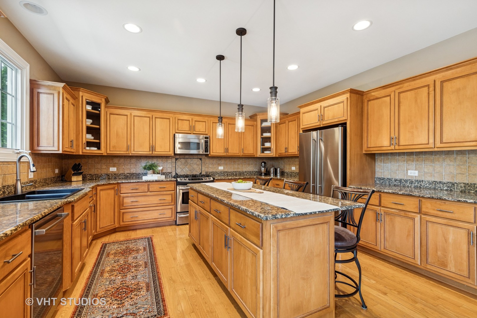 Kitchen with a large granite-topped island, honey-toned cabinets, and stainless steel appliances.