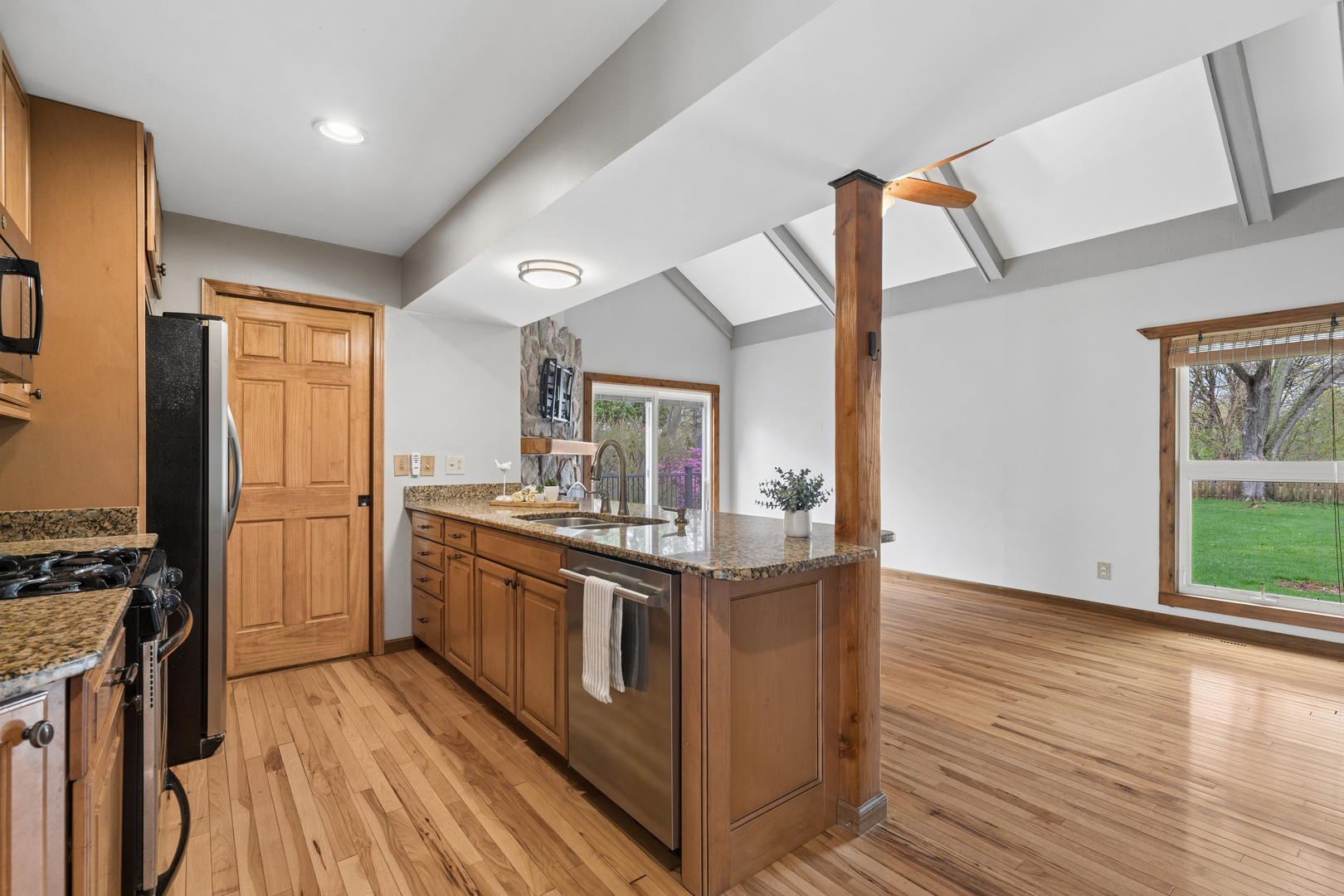Kitchen with granite island, wood cabinetry, hardwood floors, and a vaulted ceiling.