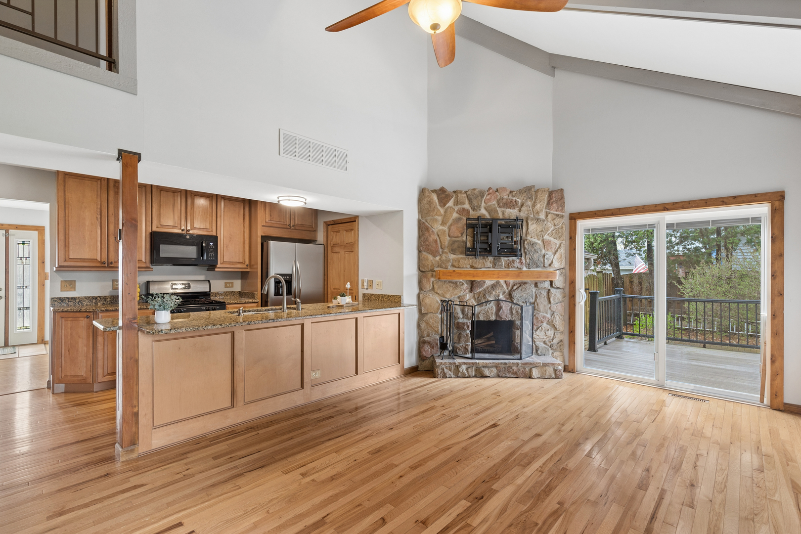 Open kitchen and living area with a stone fireplace, hardwood floors, and sliding doors to a deck.