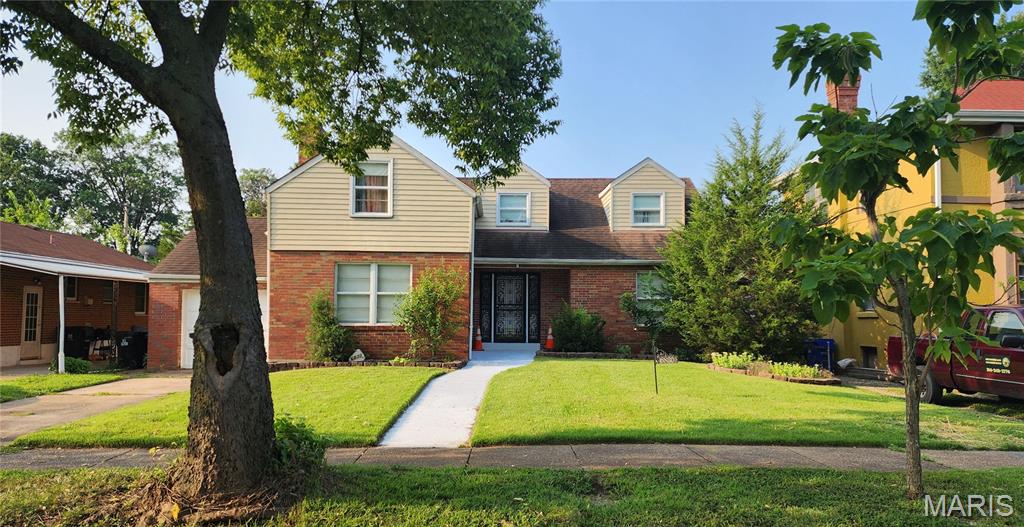 Two-story brick and beige house with dormer windows, black entry door, and a tree-shaded front lawn.