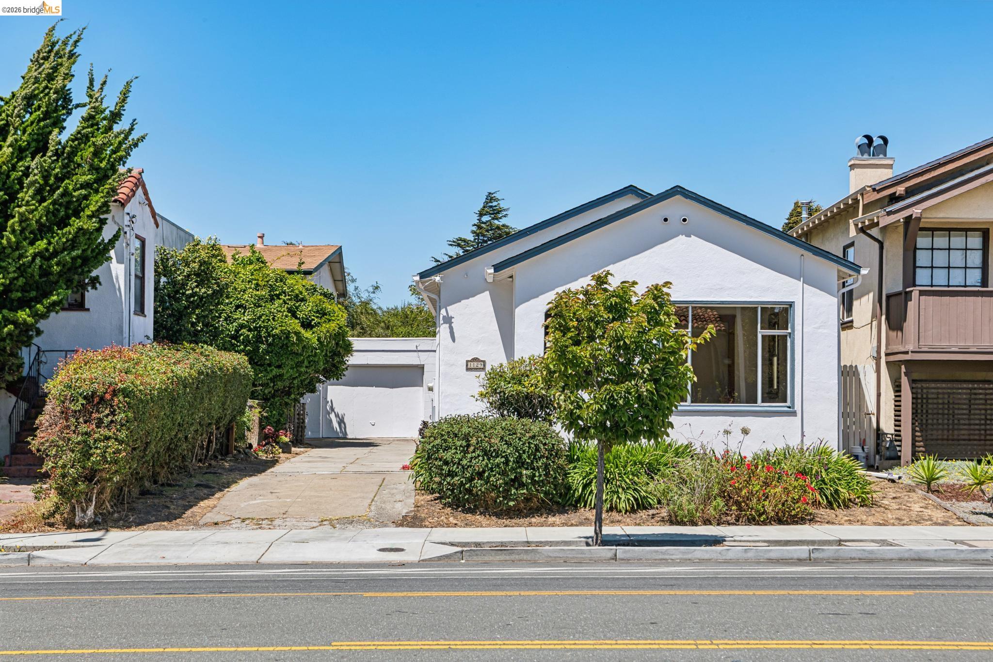 White stucco home with an attached garage, driveway, and leafy front garden.