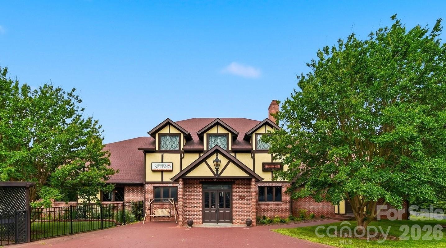Tudor-style brick building with three dormers, a paved driveway, and leafy landscaping.