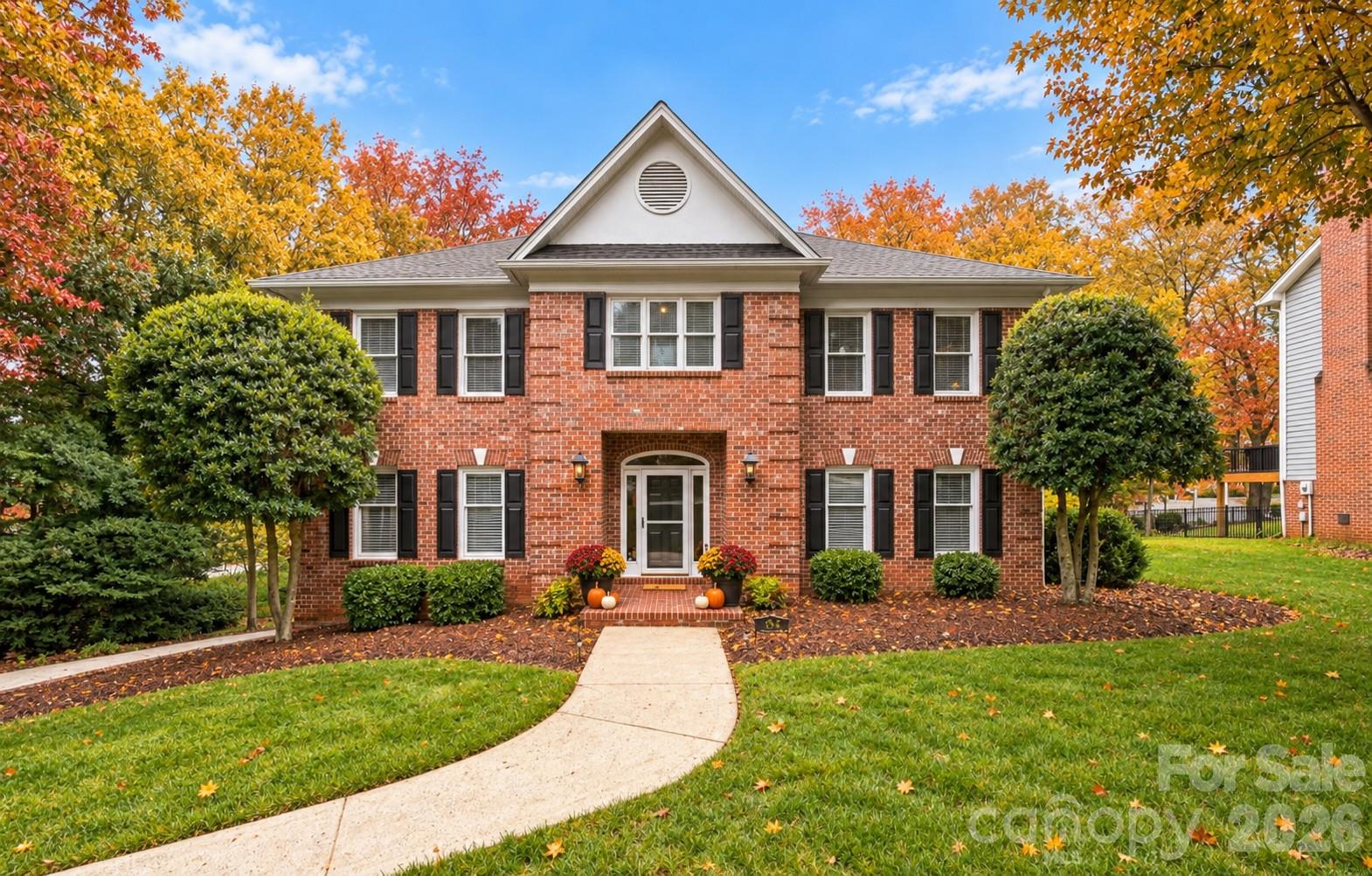 Two-story brick home with black shutters, a curved front walkway, and autumn foliage.