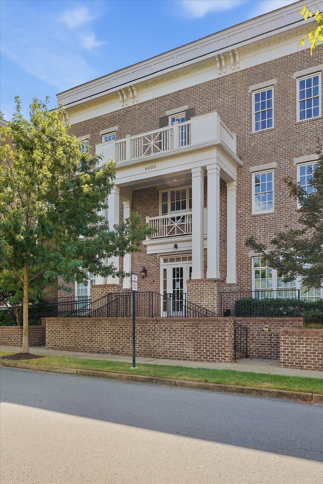 Brick condominium building with white entrance columns, balconies, and a raised courtyard.