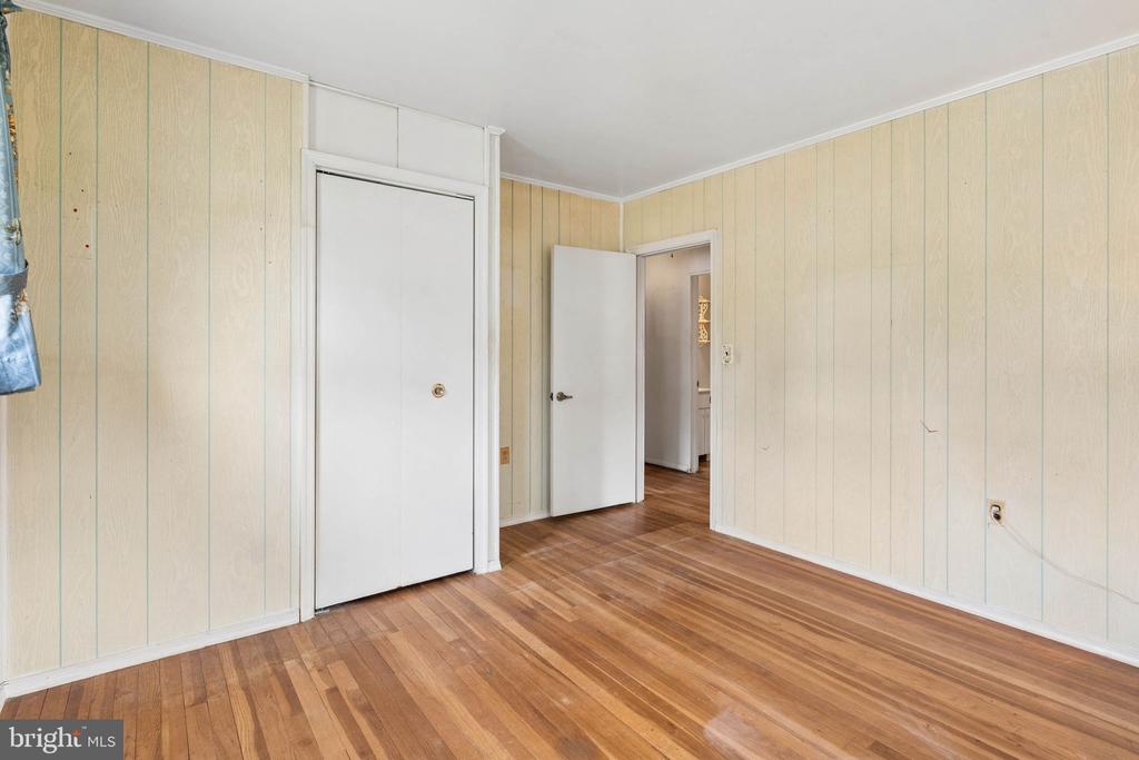 Empty room with pale paneled walls, hardwood floors, and two white doors.