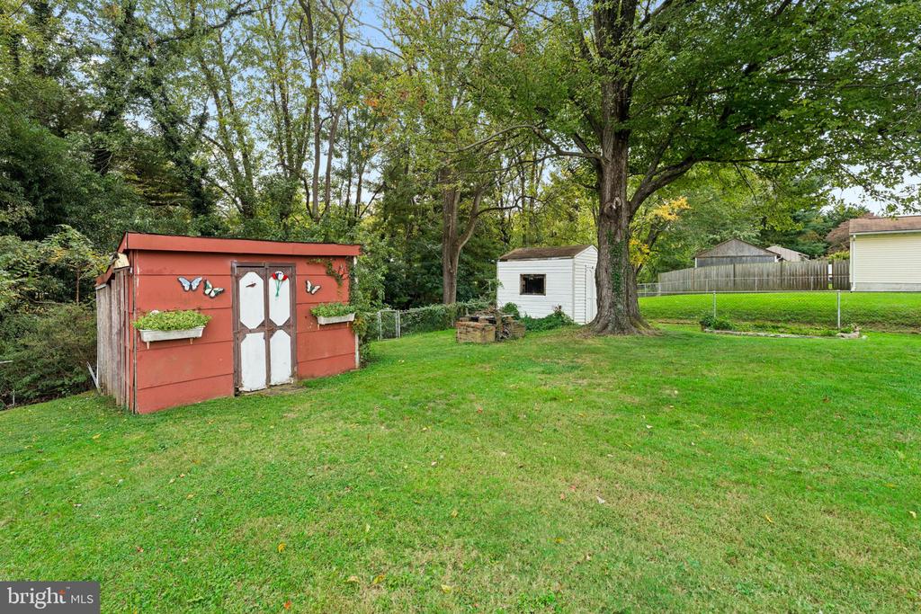 Backyard with a red garden shed, white outbuilding, and mature trees.