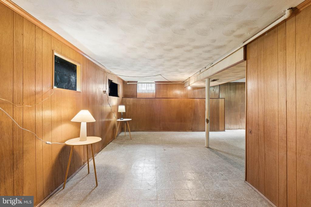 Wood-paneled basement rec room with tile flooring, two small tables, and lamps.