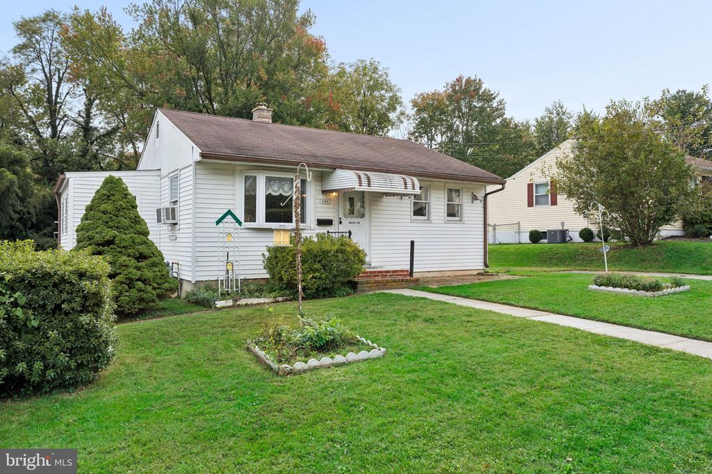 White single-story house with a striped entry awning, front lawn, and garden beds.