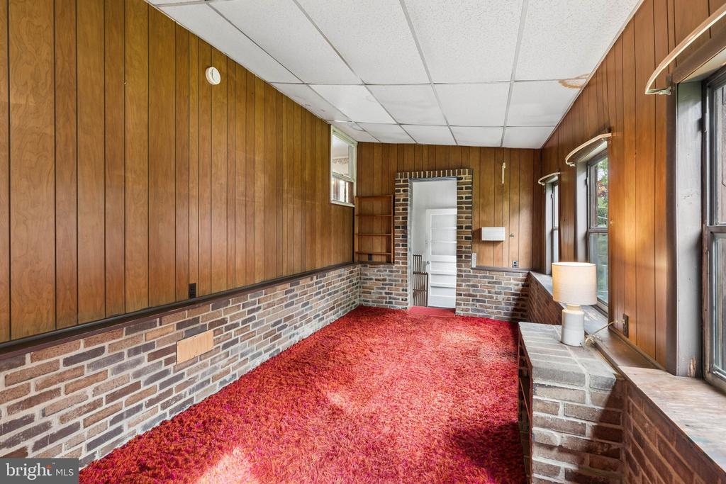 Enclosed sunroom with wood-paneled walls, brick wainscoting, and red shag carpeting.