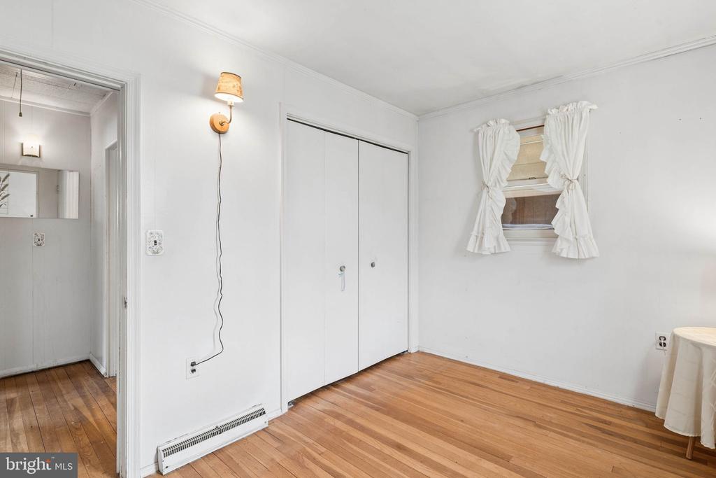 An empty bedroom with hardwood floors, a double-door closet, and a curtained window.