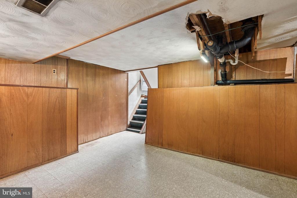 Unfinished basement with wood-paneled walls, stairway, and exposed ceiling plumbing.