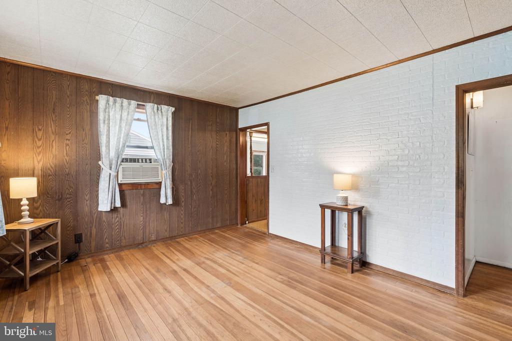 Living room with wood-paneled walls, a white brick accent wall, and hardwood floors.