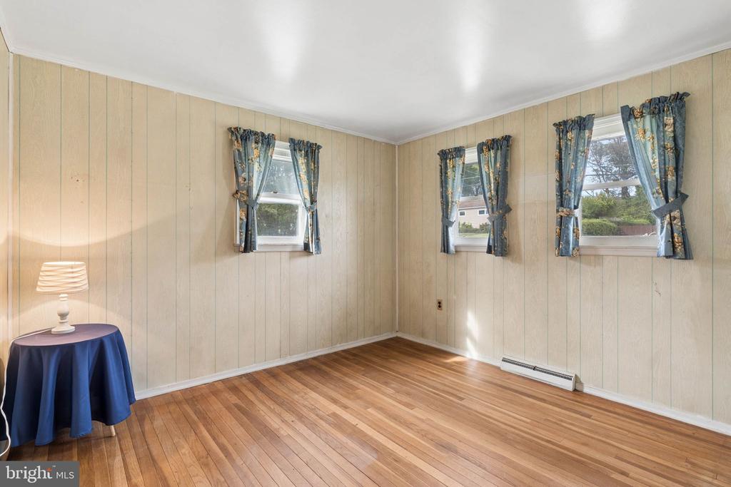 Bright room with wood floors, paneled walls, three curtained windows, and a small table with a lamp.