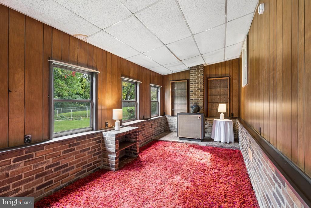 Enclosed sunroom with wood-paneled walls, brick accents, large windows, and red carpet.