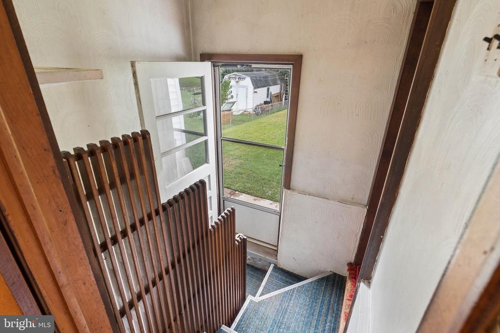 Entryway with a wooden stair railing and a glass-paneled door opening onto the yard.