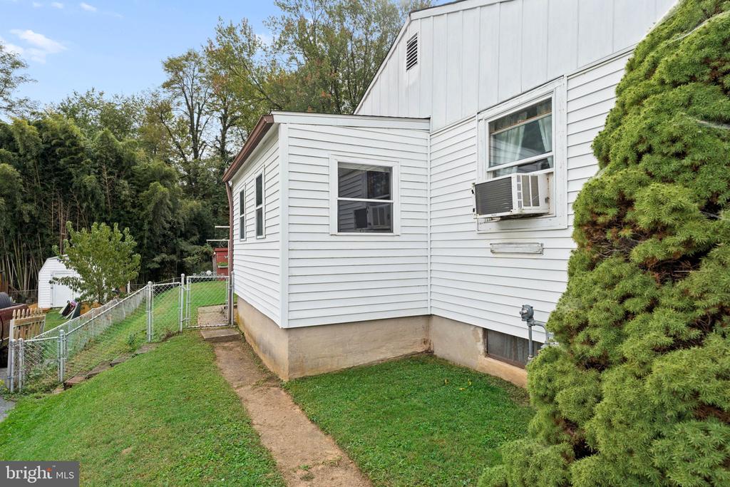 Side of a white-sided house with window air conditioners, a fenced yard, and a narrow path.