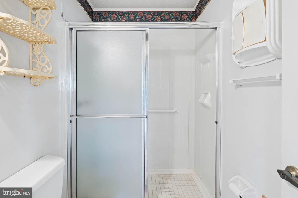 Bathroom shower with frosted sliding doors, a tiled floor, and decorative wall shelving.