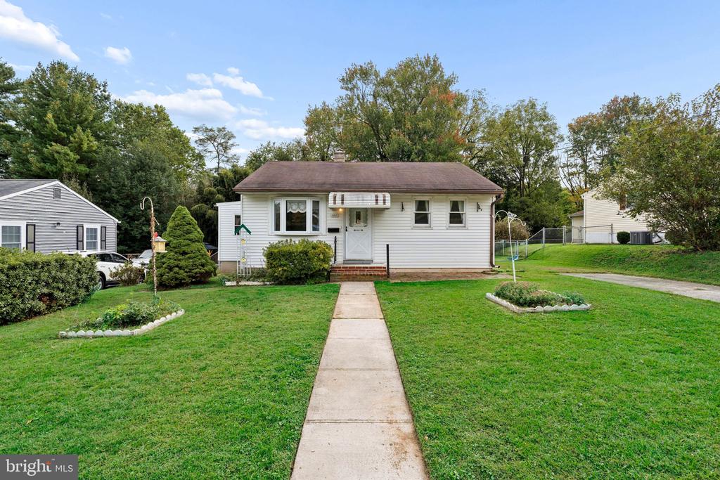 Single-story white house with a front walkway, lawn, and mature trees.