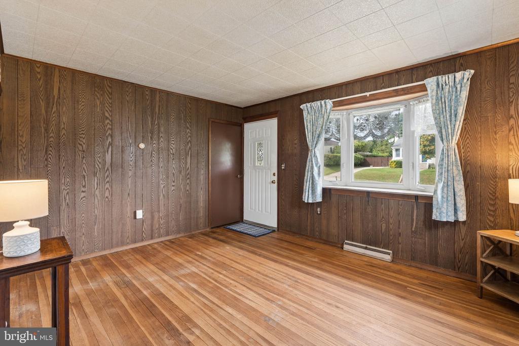 Room with wood-paneled walls, hardwood floors, and a window overlooking the front yard.