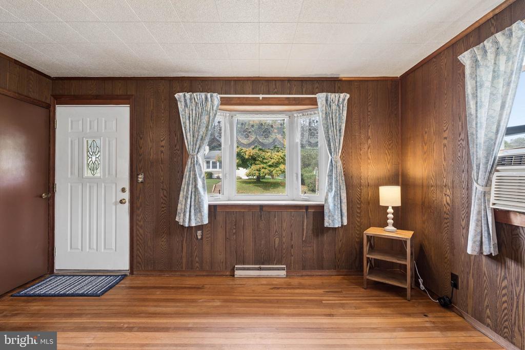 Wood-paneled room with a bay window, hardwood floors, and a white entry door.