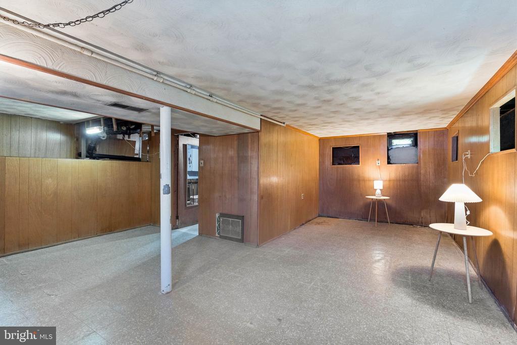 Unfurnished basement room with wood-paneled walls, a low ceiling, and two small tables with lamps.