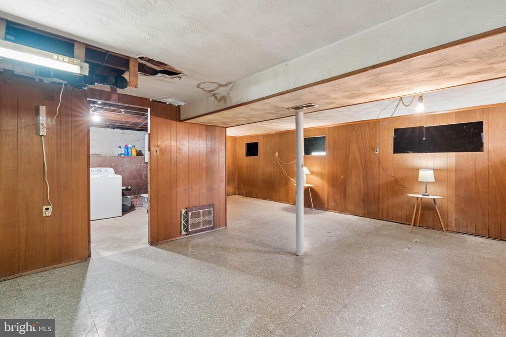 Unfinished basement with wood-paneled walls, exposed ceiling damage, and a laundry area.