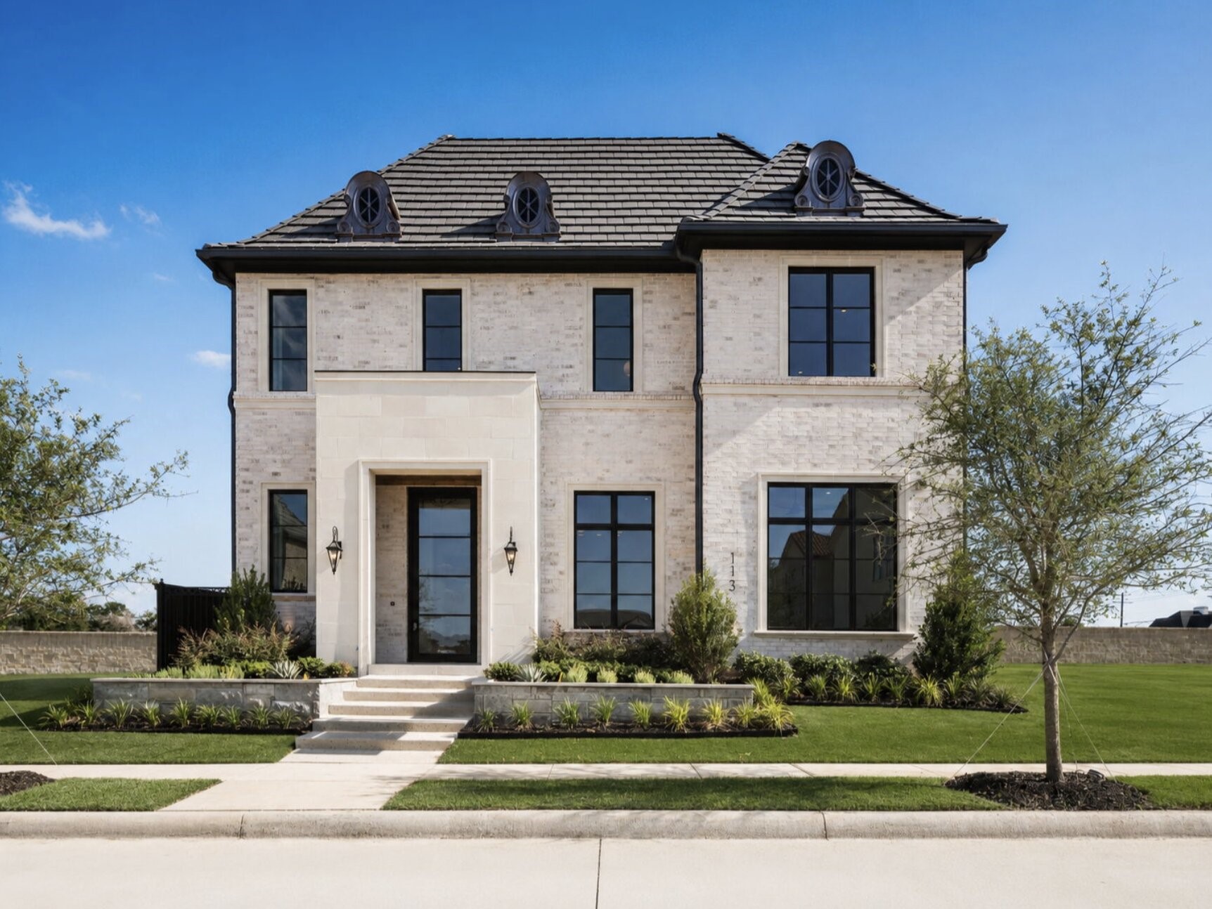 Two-story light brick home with a dark tiled roof, black-framed windows, and landscaped front lawn.