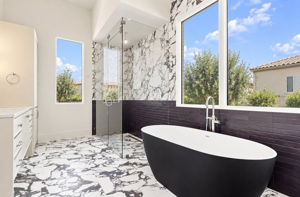 Modern bathroom with a freestanding tub, glass shower, marble-patterned tile, and large sunny window.