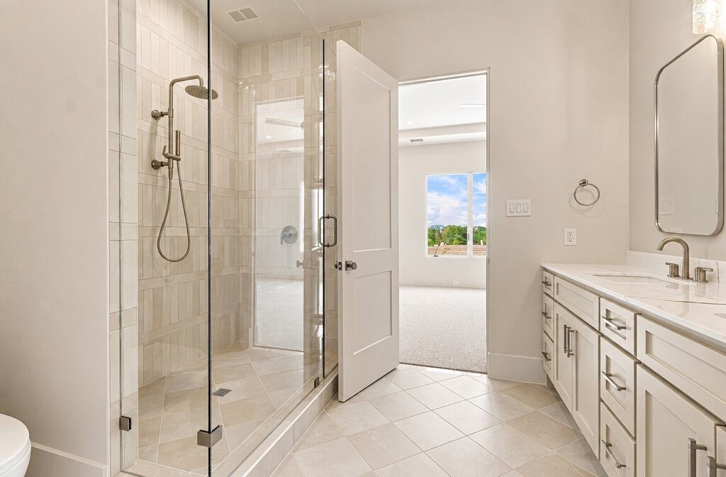 Bathroom with glass-enclosed walk-in shower and long white vanity with dual sinks.