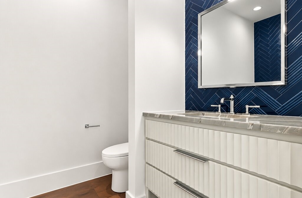 Bathroom with a white fluted vanity, marble counter, and dark blue herringbone tile backsplash.