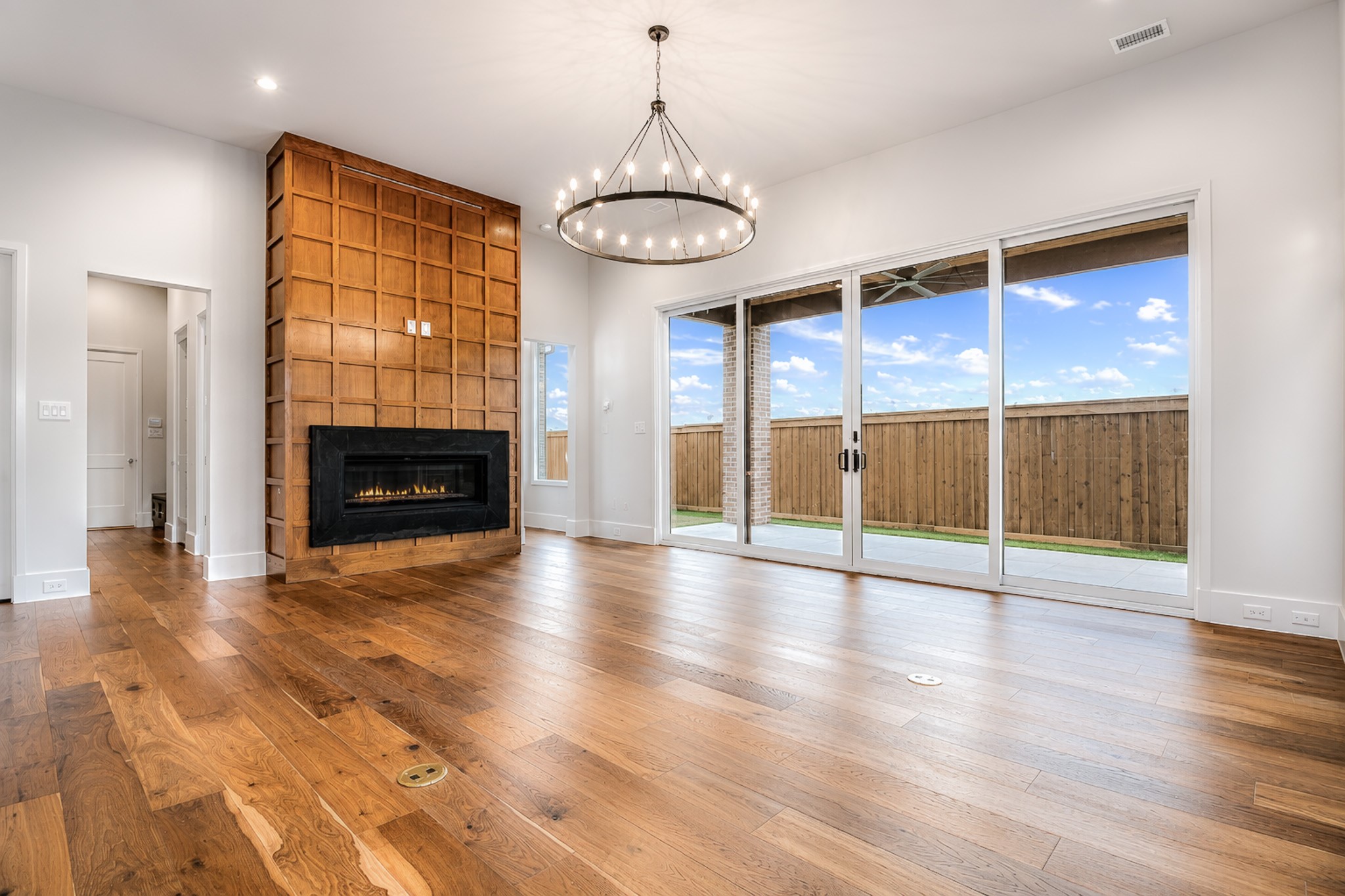 Vacant living room with a wood-paneled fireplace wall, hardwood floors, and sliding doors to a fenced patio.