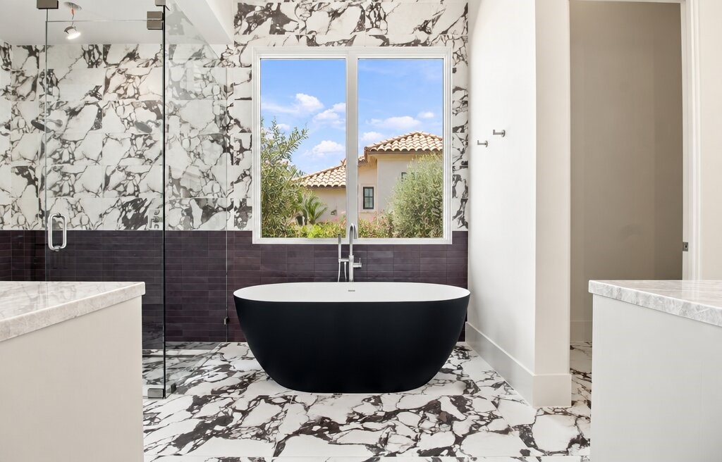 Modern bathroom with a black freestanding tub, marble-patterned walls, and a window overlooking the neighboring home.